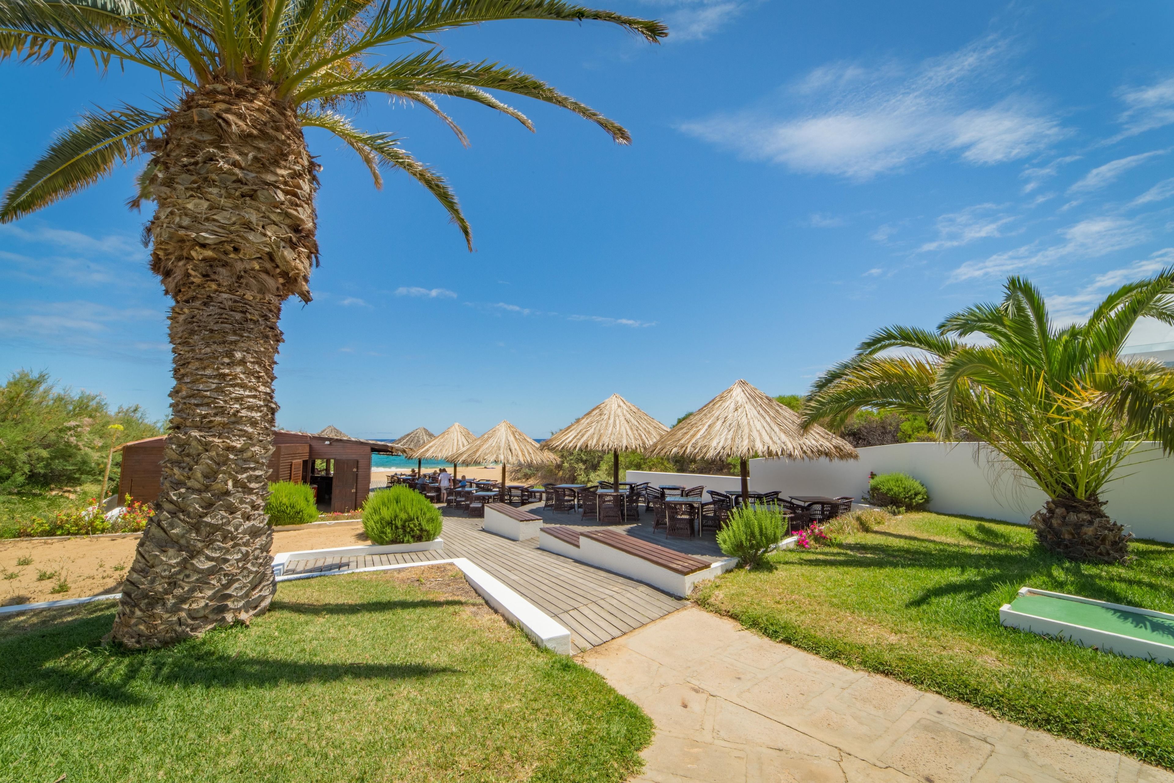 A resort with outdoor seating, palm trees, and thatched umbrellas.