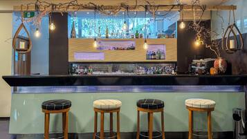 Un espace bar avec des tabourets en bois, des luminaires suspendus et une variété de bouteilles et de verres exposés sur des étagères.