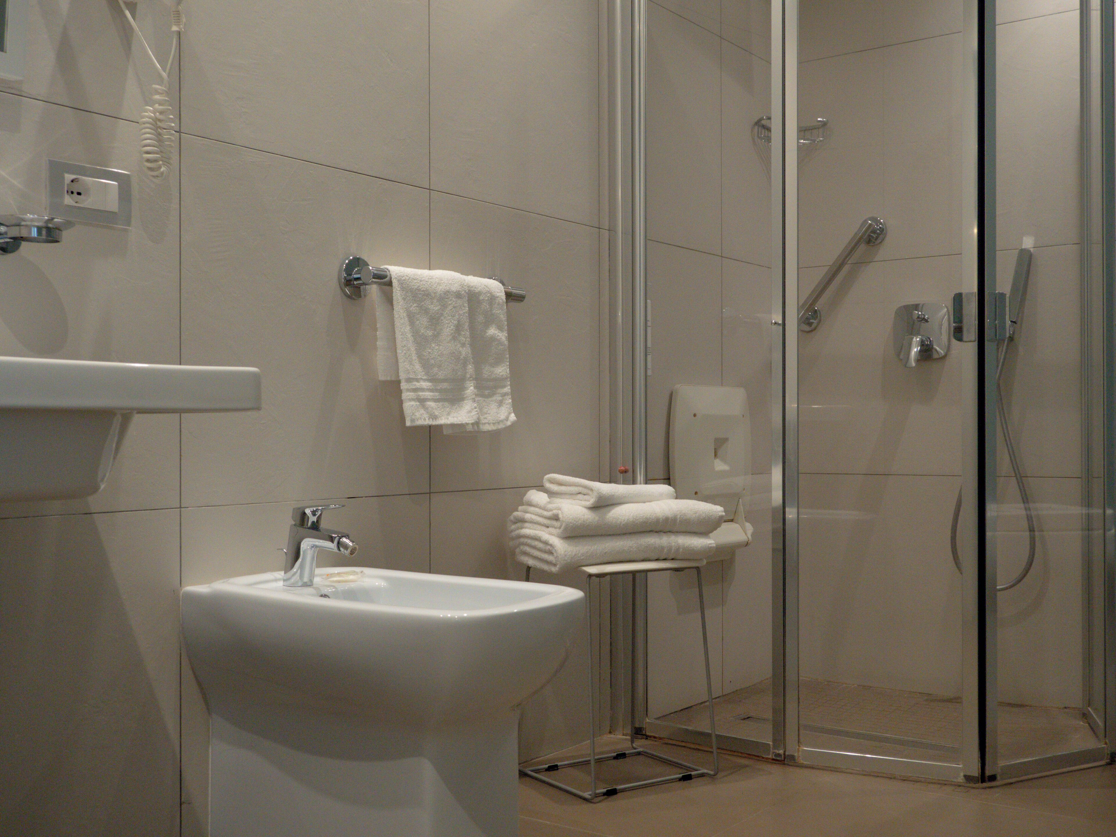 A modern bathroom with a glass-enclosed shower, a sink, and neatly stacked towels.