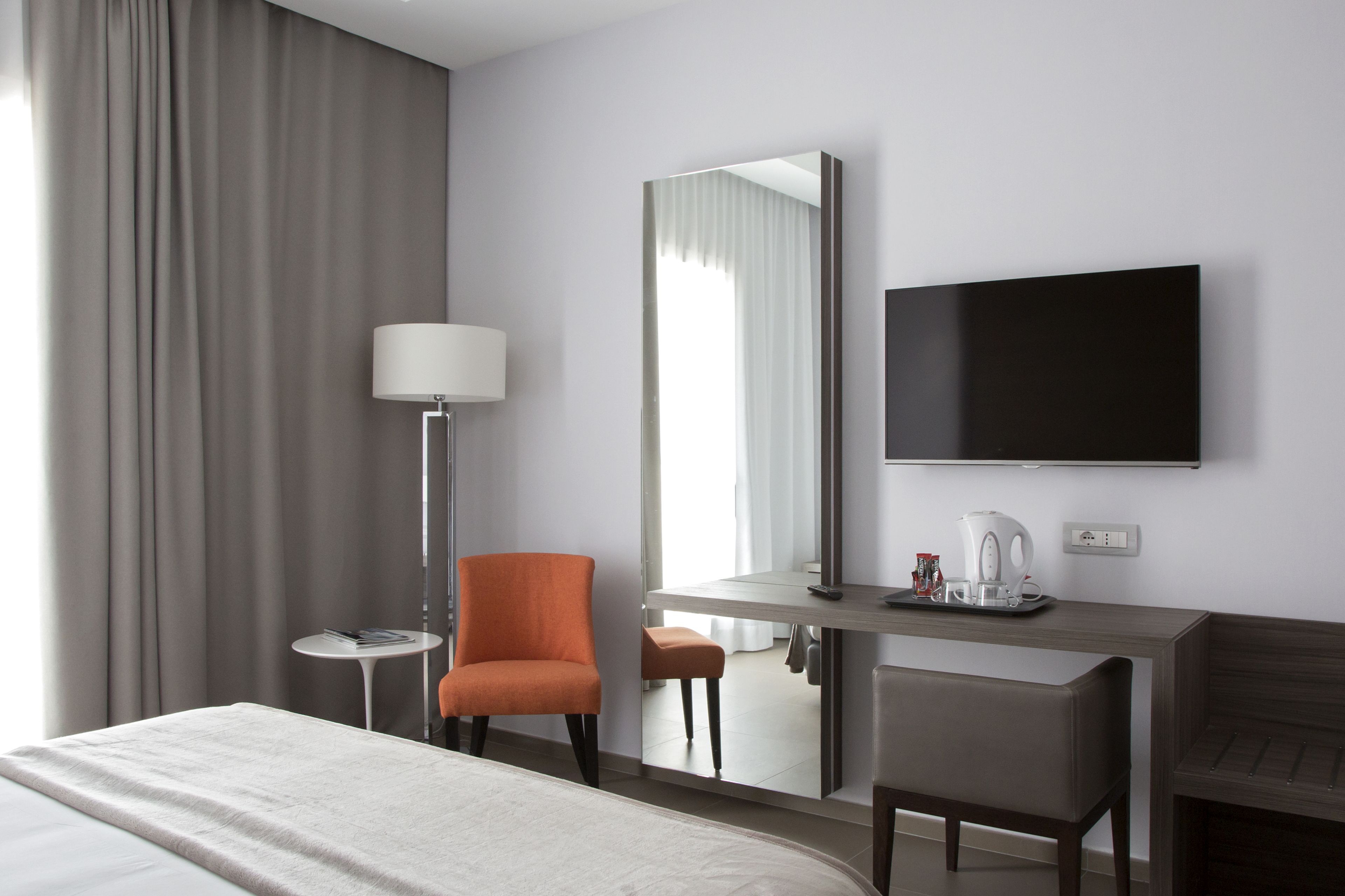 Une chambre d’hôtel comprenant un lit, un bureau avec une chaise, une télévision, une lampe et une fenêtre avec des rideaux.