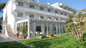 Un hotel de varios pisos con una zona de estar exterior cubierta, una escalera y plantas en macetas.