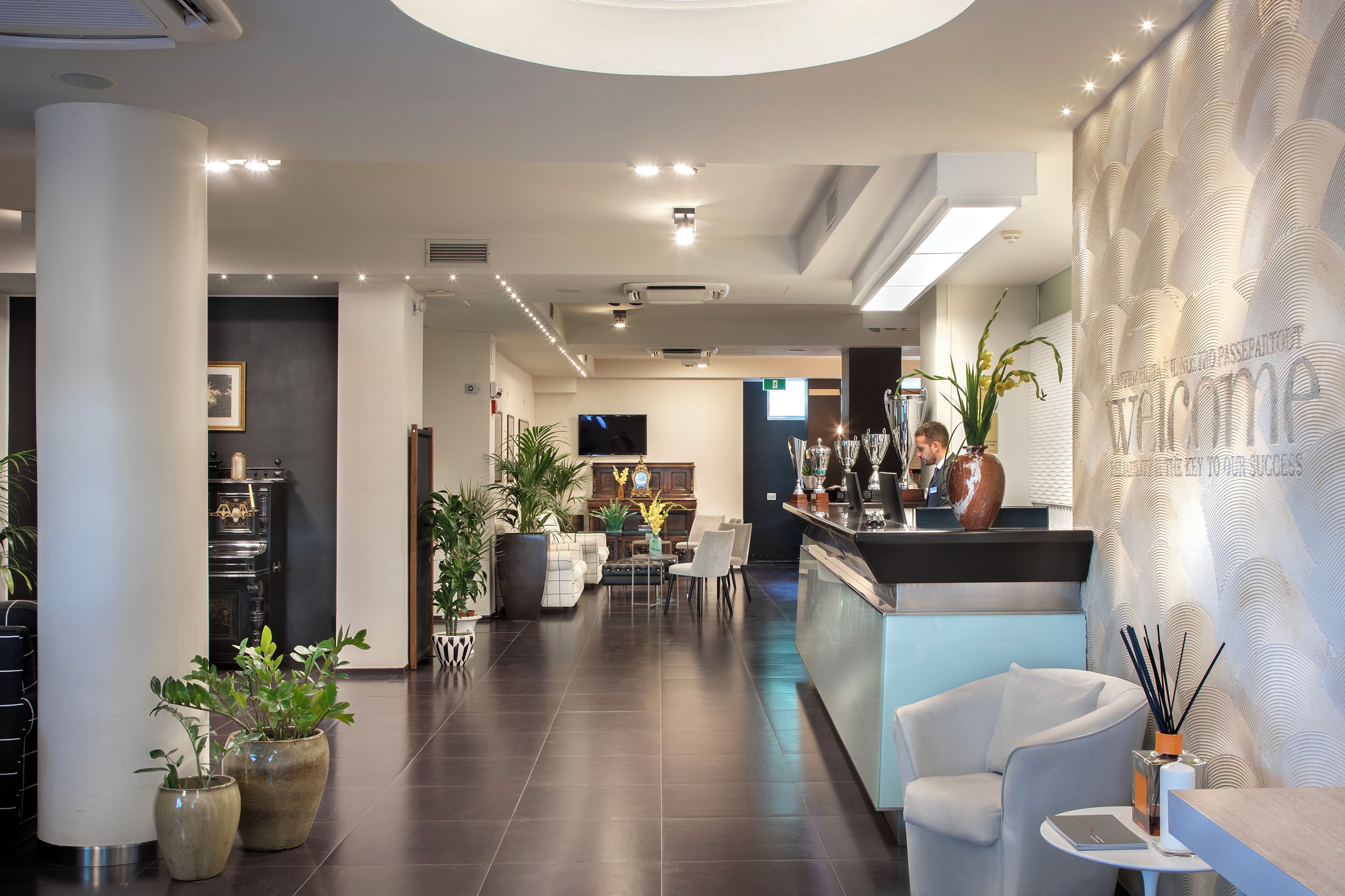 A hotel lobby with a reception desk, seating area, and a large plant.