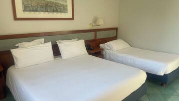 A hotel room with two beds, a nightstand, a lamp, and a framed picture on the wall.