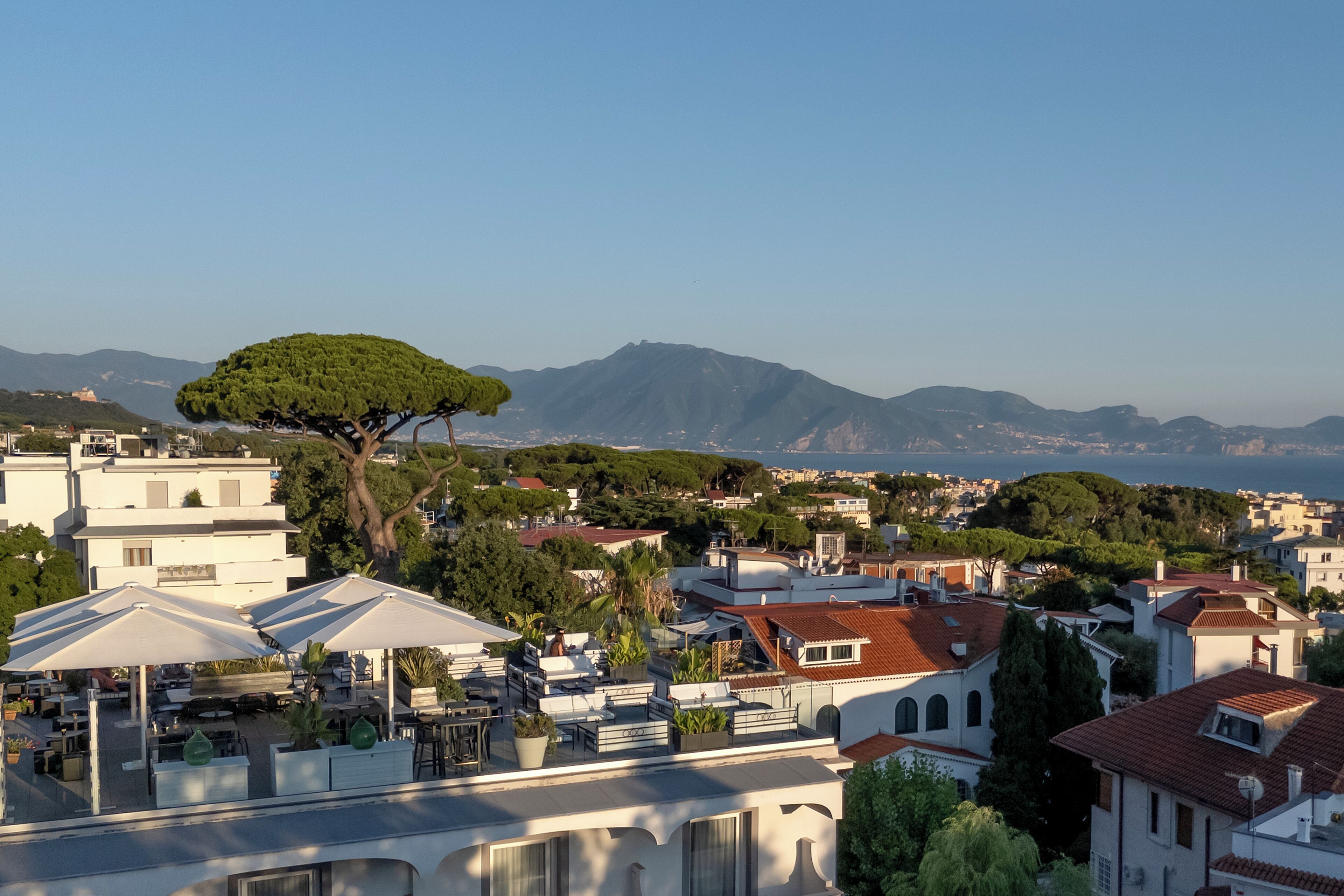 A residential area with a prominent tree, buildings with varied architecture, and a distant mountain range.
