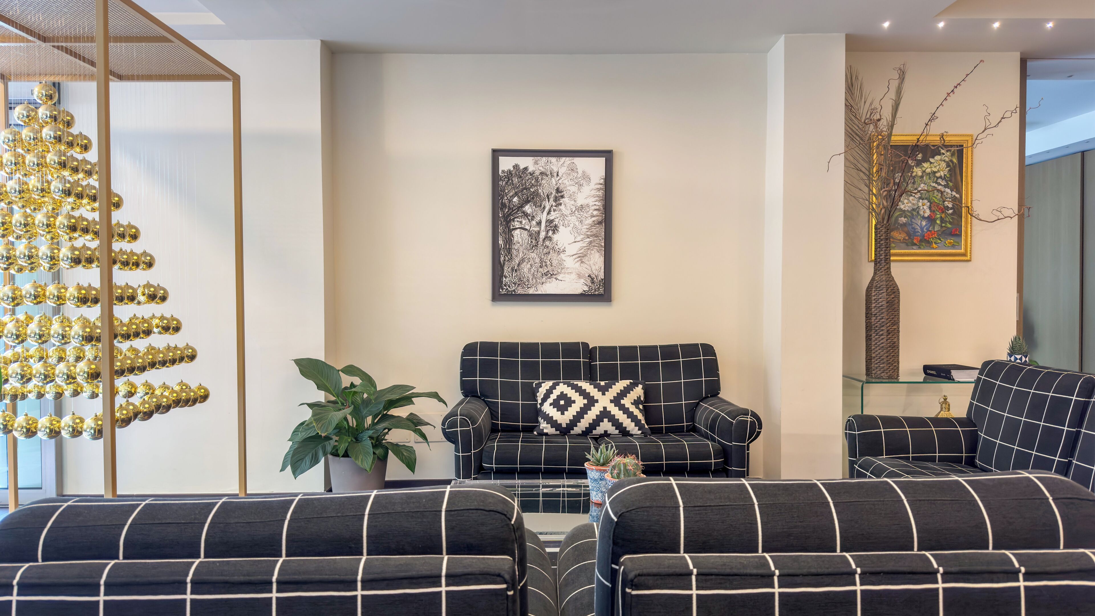 A modern living room with a sofa set, a decorative plant, and a framed artwork on the wall.