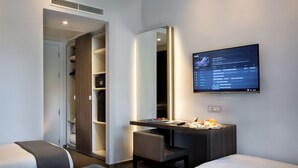 Una habitación de hotel moderna con una cama, un escritorio con computadora, una televisión y un armario.