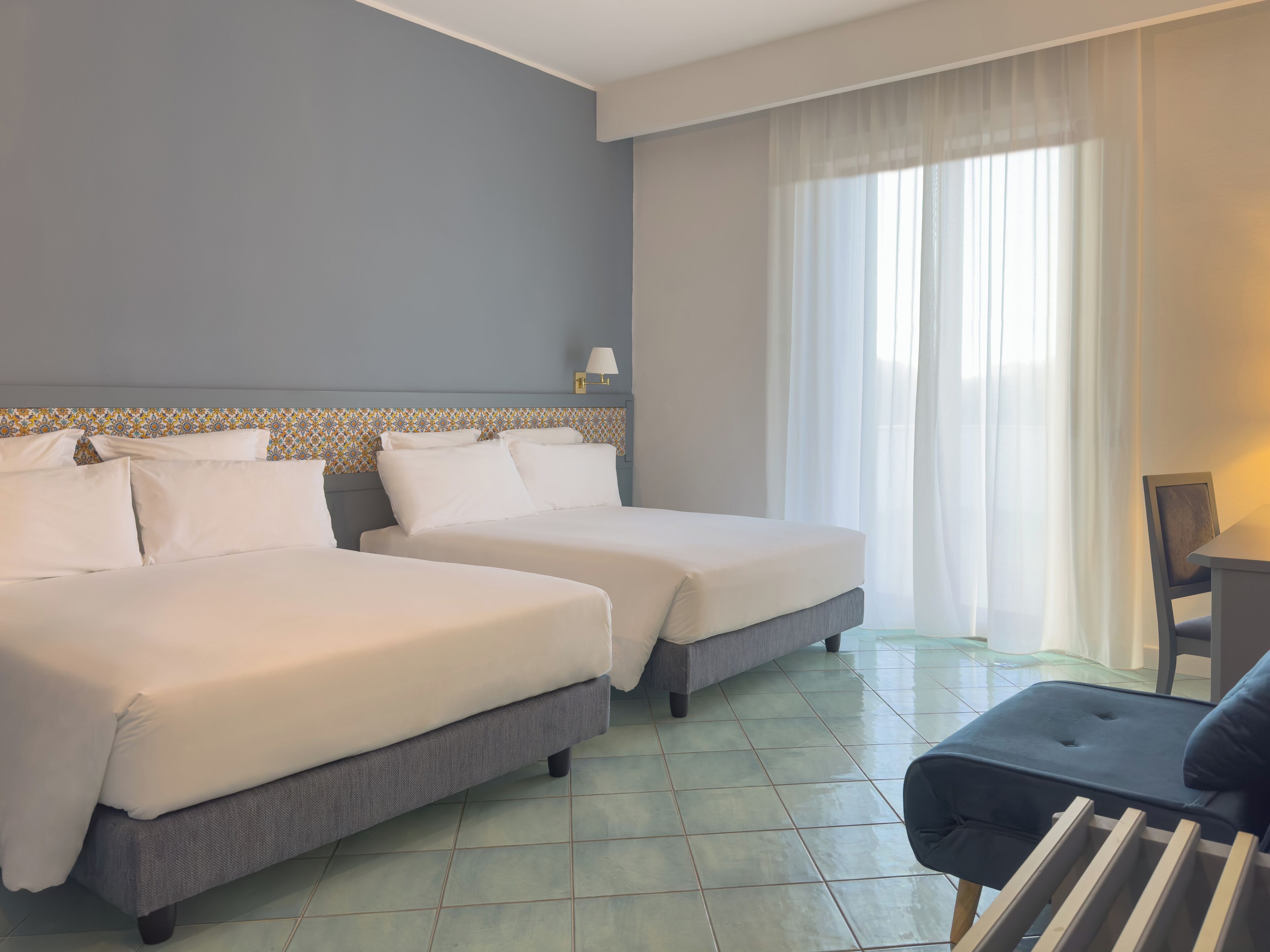 A hotel room with two beds, a chair, a table, and a window with curtains.