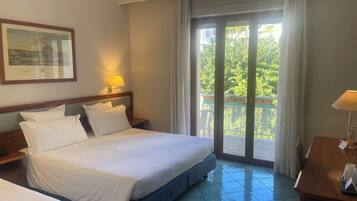 A hotel room with a bed, a desk, and a balcony with a view of greenery.