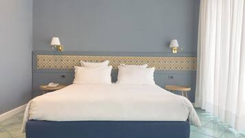 Una cama bien tendida con sábanas blancas, cabecera azul y un salpicadero de azulejos estampados. Hay dos mesitas de noche, una con lámparas y un teléfono.