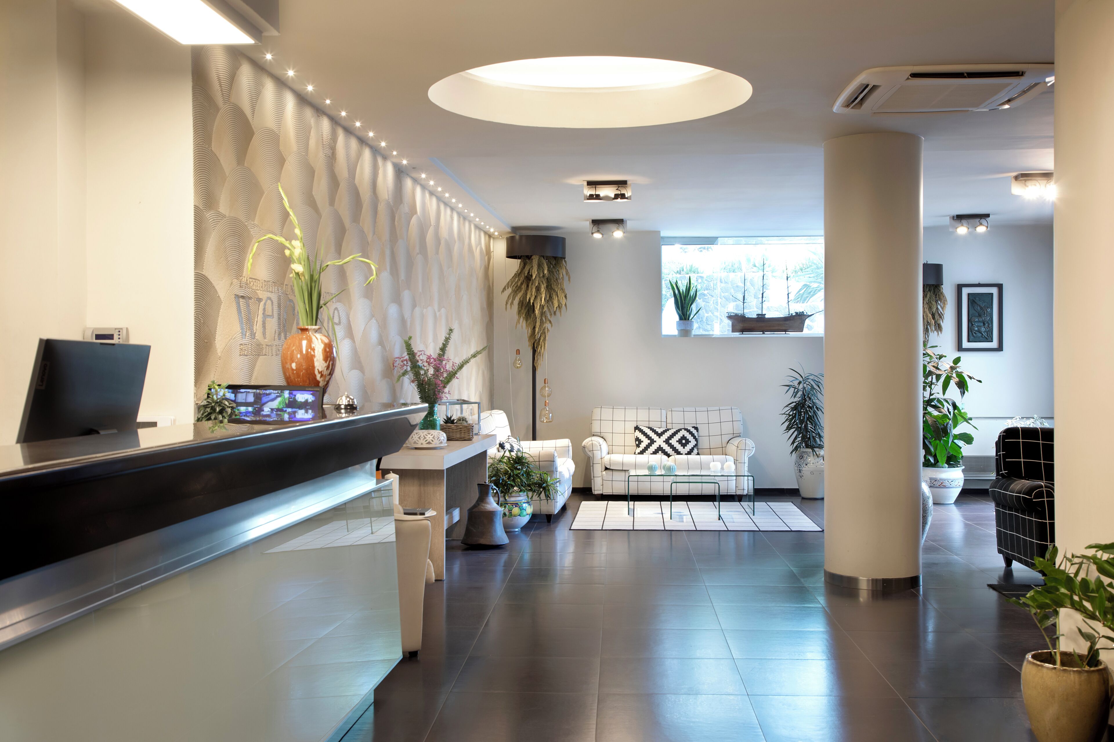 Un área de recepción moderna con mostrador, asientos y plantas decorativas.