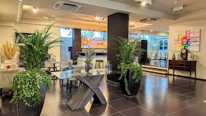 Un moderno vestíbulo de hotel con una mesa de centro de vidrio, plantas en macetas y una recepción.