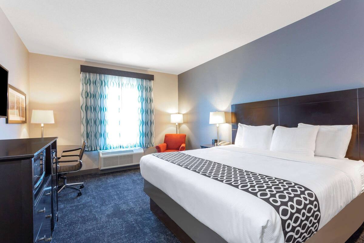 Une chambre d’hôtel avec un grand lit, un bureau, une chaise et une fenêtre avec des rideaux.