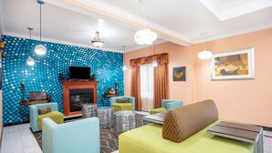 A living room with a blue polka dot wall, a fireplace, and a television. There are several sofas and a coffee table. - La Quinta Inn & Suites by Wyndham St. Augustine (St. Augustine)