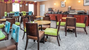 A hotel dining area with multiple tables and chairs, a kitchen area with appliances, and a door leading outside. - La Quinta Inn & Suites by Wyndham St. Augustine (St. Augustine)
