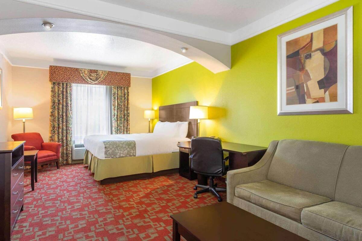Une chambre d’hôtel avec un lit, un bureau, une chaise, un canapé et un tableau au mur.