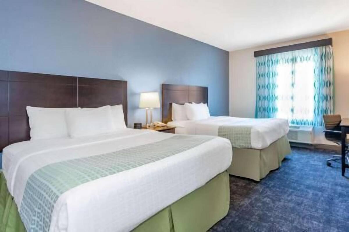 Une chambre d’hôtel avec deux lits, un bureau, une chaise et une fenêtre avec des rideaux.