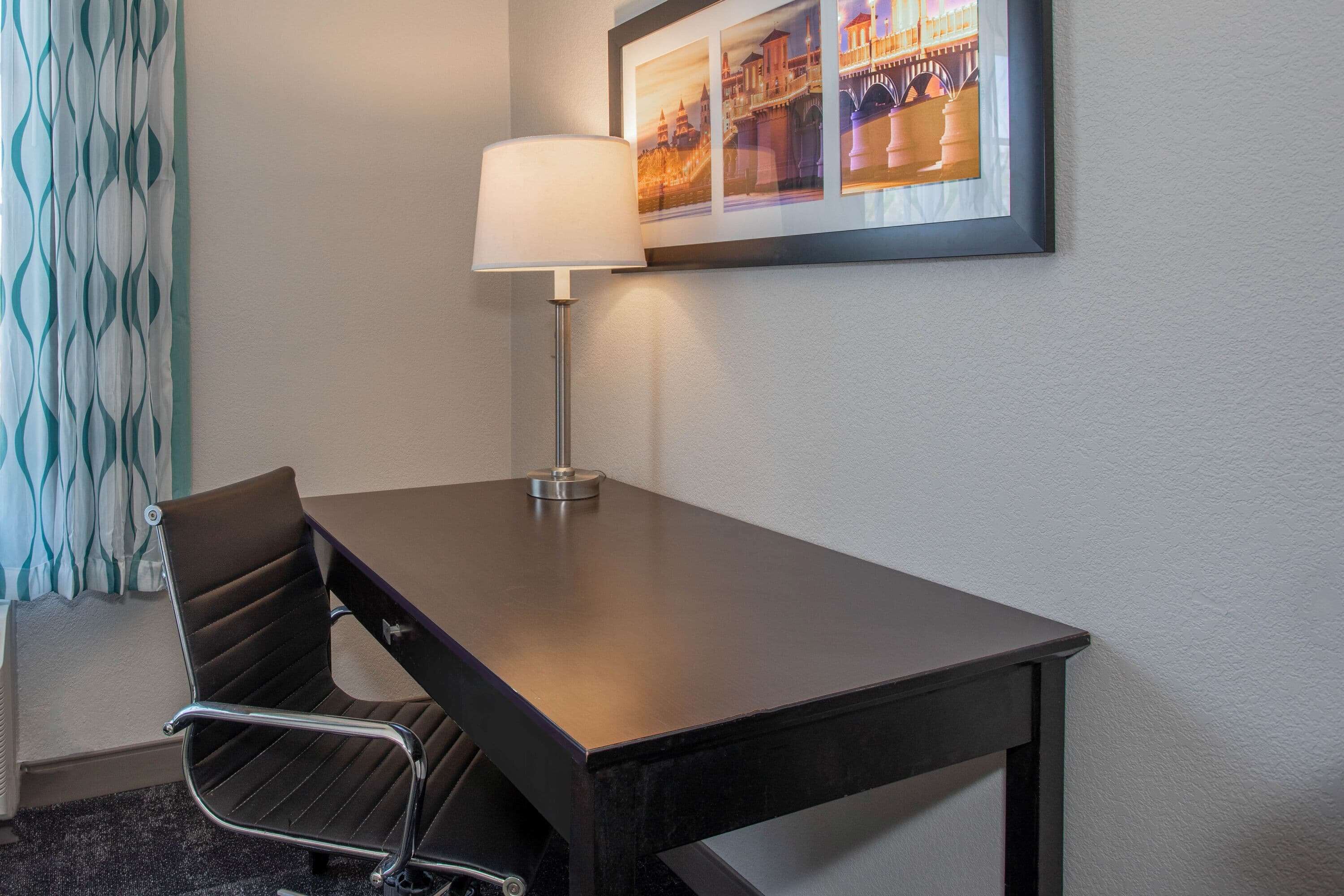 Une chambre d’hôtel avec un bureau en bois foncé, une chaise moderne, une lampe sur pied et un tableau encadré au mur.