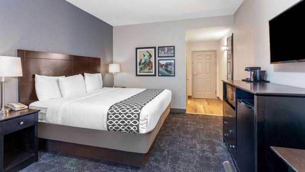 A hotel room with a large bed, bedside tables with lamps, a flat-screen TV, a kitchenette, and framed artwork on the wall. - La Quinta Inn & Suites by Wyndham St. Augustine (St. Augustine)