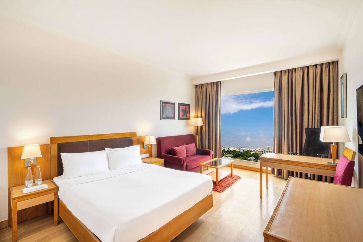 Une chambre d’hôtel avec un grand lit, un bureau, une chaise, un canapé et une vue sur la ville.