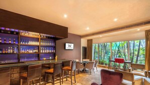 Una zona de bar con una variedad de botellas de licores, una pantalla de televisión y asientos que incluyen taburetes y una mesa redonda.