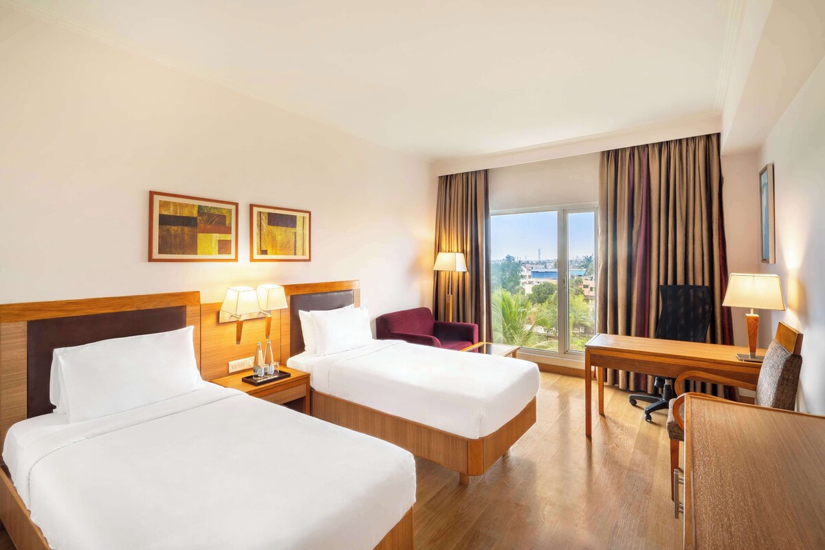 Habitación de hotel con dos camas, un escritorio, una silla y vistas a la ciudad.