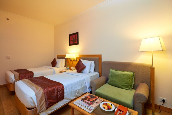 A hotel room with two beds, a sofa, a table with a newspaper, and a lamp.
