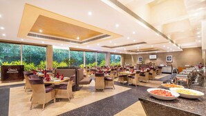 Un restaurante espacioso con varias mesas y sillas, amplias ventanas que ofrecen vistas a zonas verdes y una zona de bufé con diversas opciones de comida.