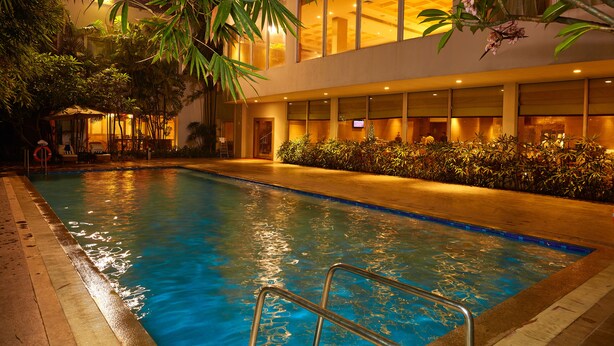 Una piscina interior con superficie de agua cristalina, rodeada de exuberante vegetación y un edificio moderno con amplias ventanas.