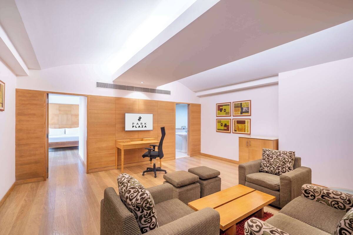Un salon moderne avec un bureau en bois, un canapé et une table basse. Un panneau est accroché au mur, sur lequel on peut lire « PARK PLAZA ».