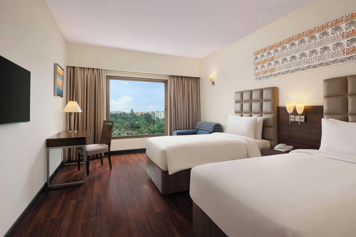 A hotel room with two beds, a desk, a chair, a window with a view, and a decorative wall piece.