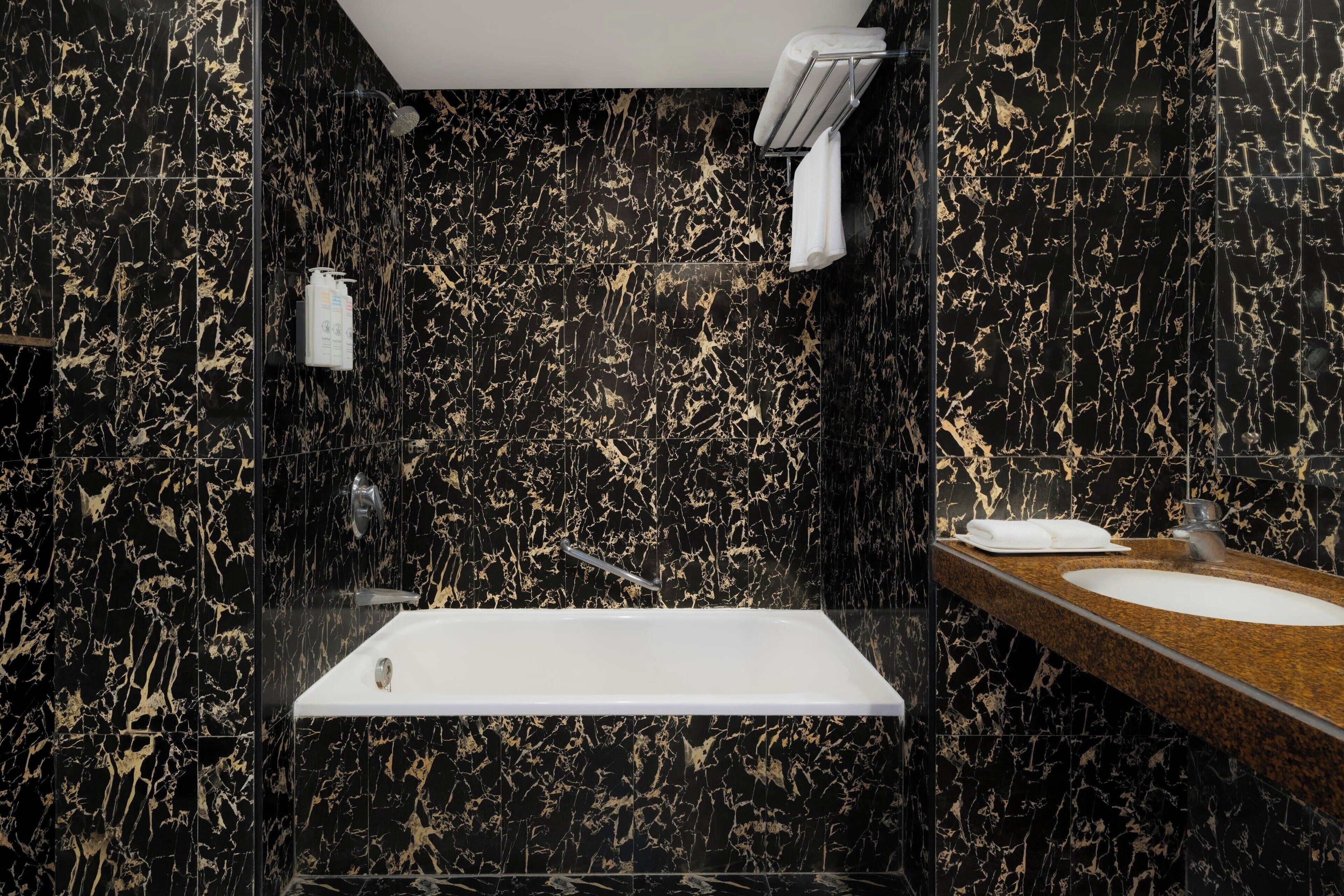 A modern bathroom with a black marble sink, a standalone bathtub, and a towel rack.