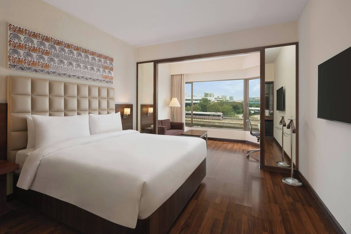 A hotel room with a large bed, a view through a sliding door, a flat-screen TV, and a decorative wall piece.