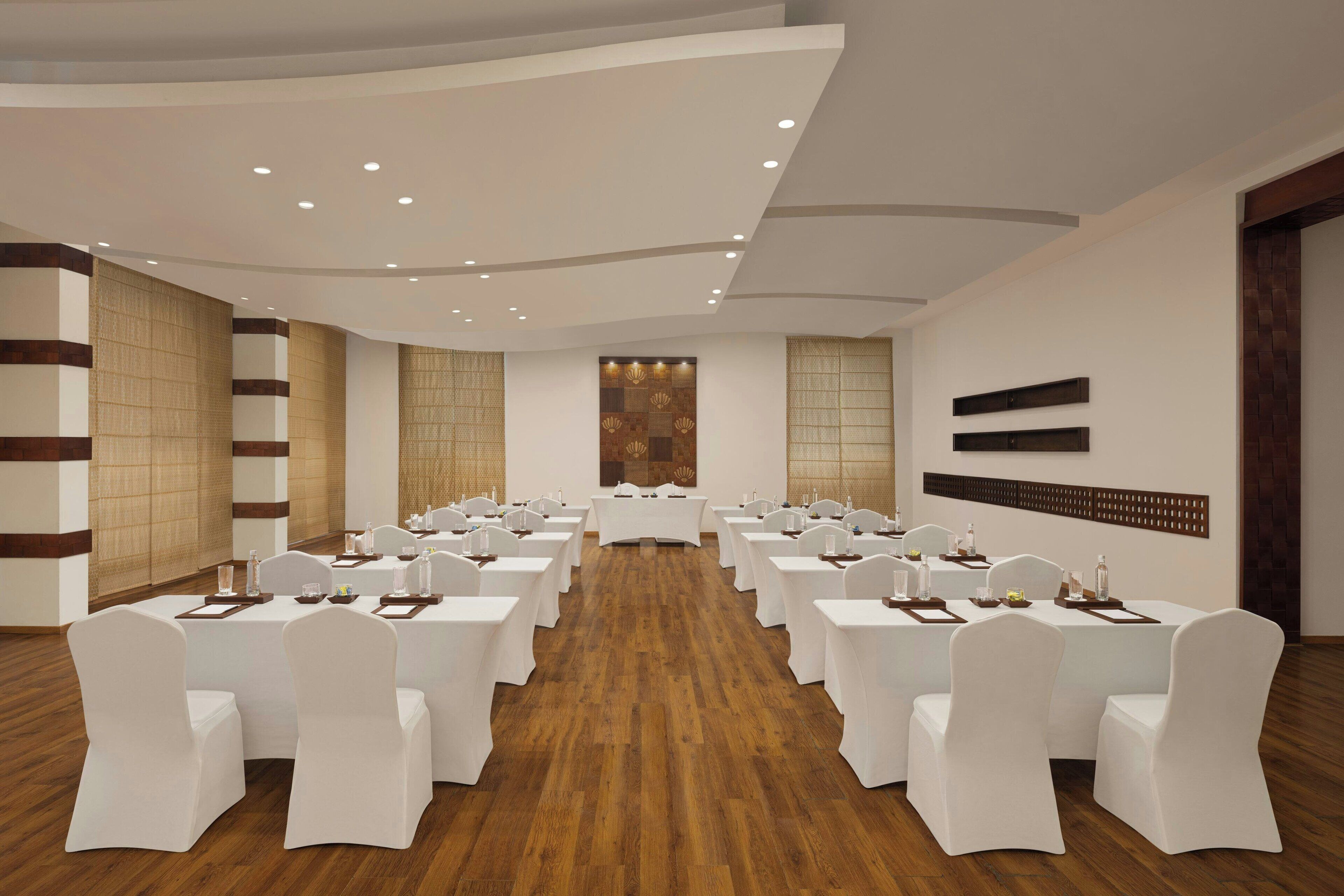 A conference room with round tables and white chairs, wooden flooring, and recessed ceiling lighting.