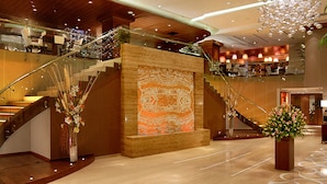 Un vestíbulo amplio con una escalera monumental, un gran panel decorativo y una zona de recepción.
