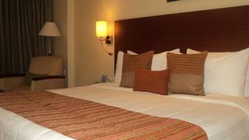 A hotel room with a large bed, a headboard, a lamp, and a chair.