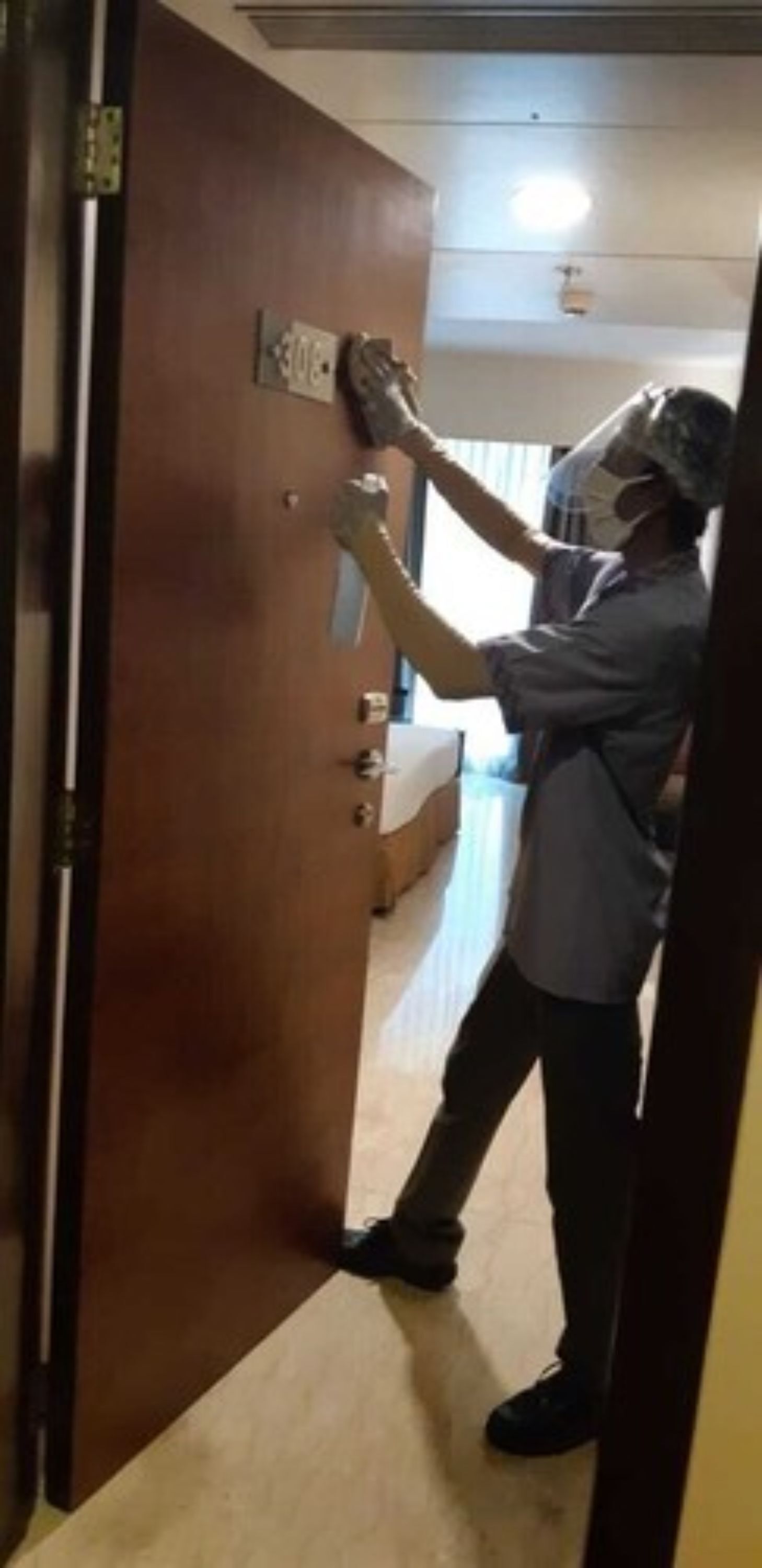 Una persona ajustando la cerradura de una puerta en una habitación con cama y ventana.
