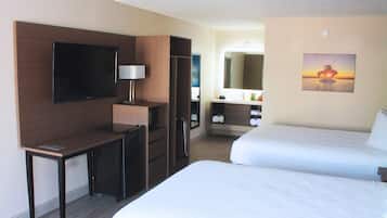 Habitación de hotel con cama, escritorio con televisor, espejo y baño con lavamanos y espejo.