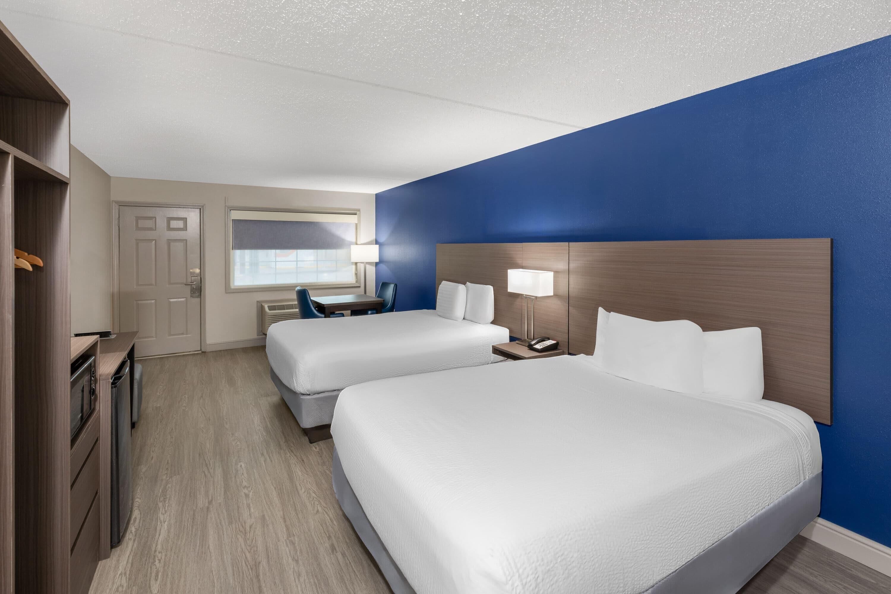 A hotel room with two beds, a desk, a chair, a wardrobe, and a window.