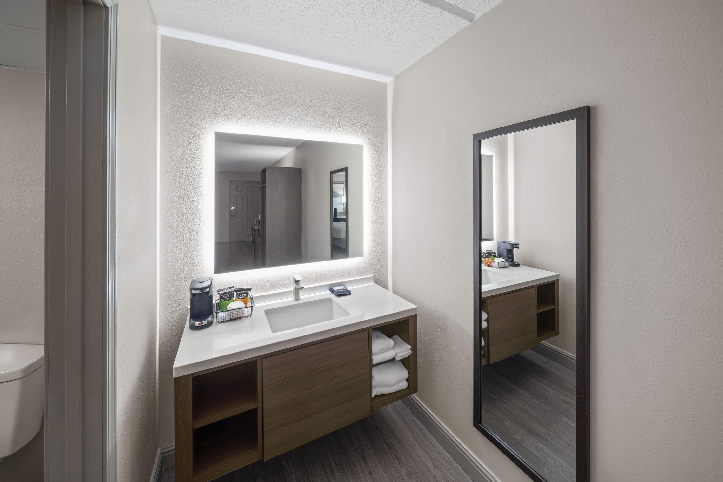 A modern bathroom with a white sink, wooden vanity, and a large mirror.