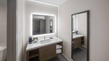 A modern bathroom with a white sink, wooden vanity, and a large mirror.
