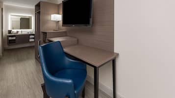 Camera d'albergo con scrivania, una sedia, televisore, specchio e bagno.