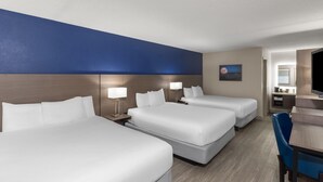 A hotel room with three beds, a desk, and a chair.