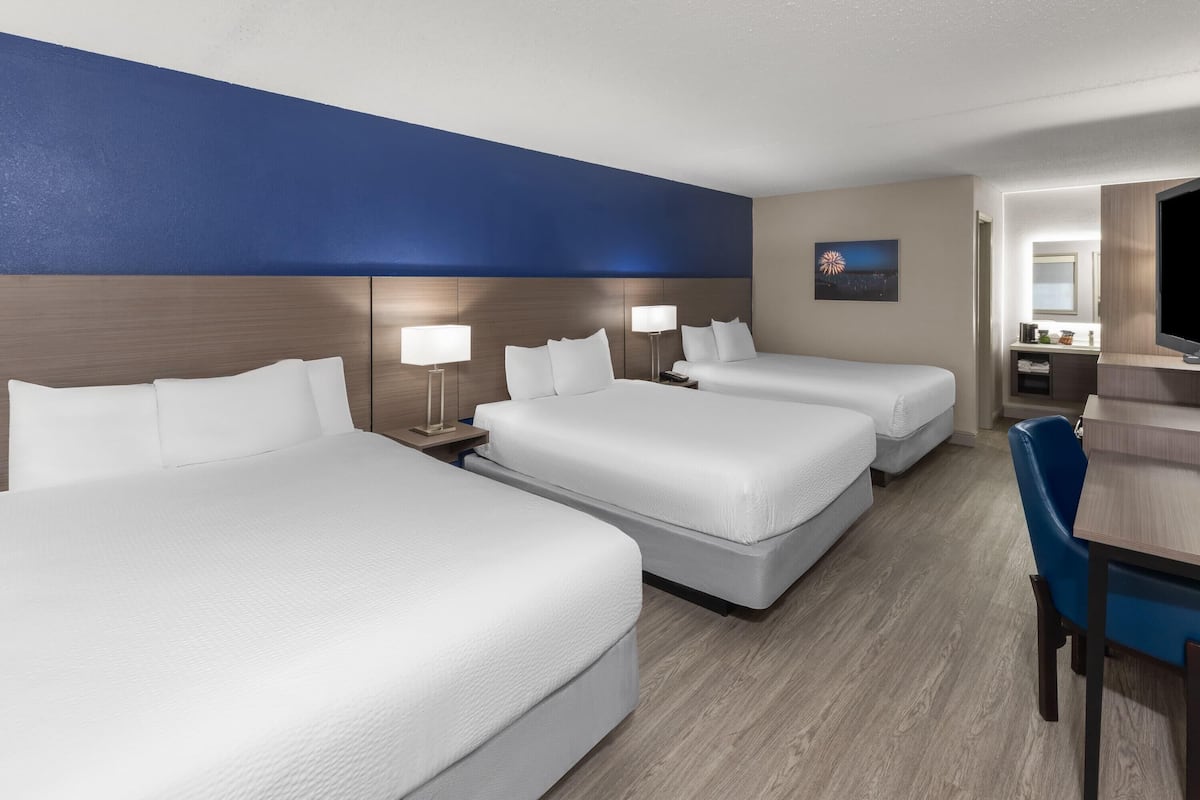 A hotel room with three beds, a desk, and a chair.