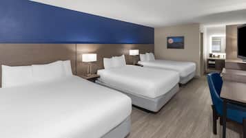 A hotel room with three beds, a desk, and a chair.