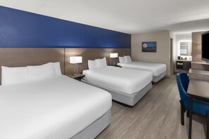 A hotel room with three beds, a desk, and a chair.