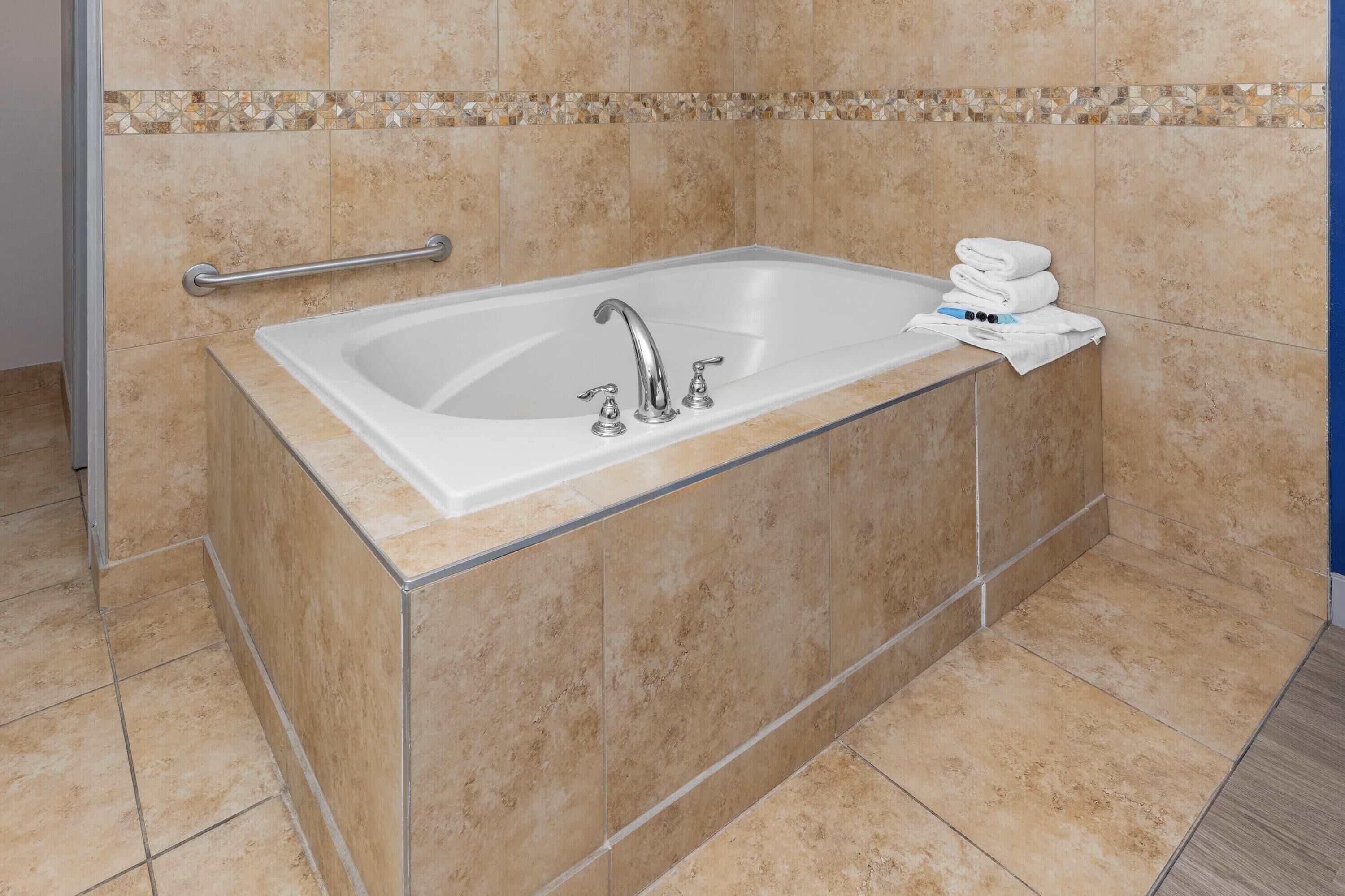 A bathroom with a bathtub, a handrail, and a stack of towels.