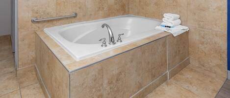 A bathroom with a bathtub, a handrail, and a stack of towels.