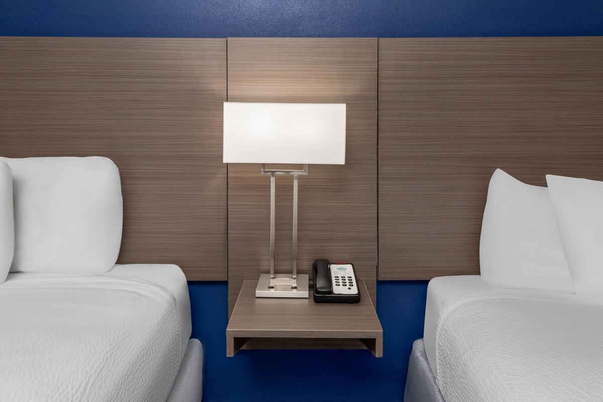 A hotel room with two beds, a bedside table with a lamp and phone, and a wooden headboard.