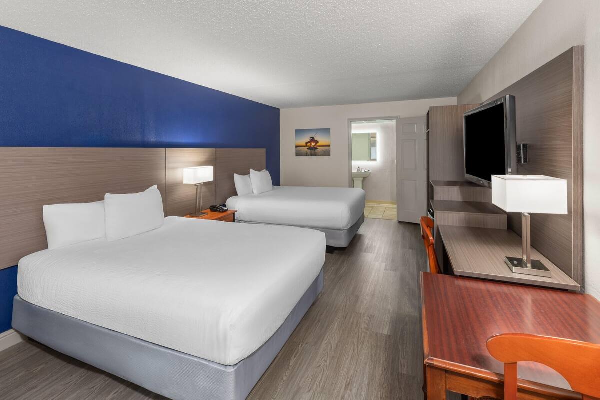 A hotel room with two beds, a desk, a TV, and a bathroom visible through an open door.