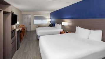 A hotel room with two beds, a desk, a chair, a TV, and a window.